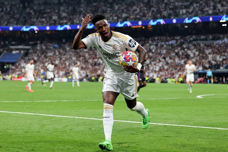 Jogador de futebol com uniforme branco segura bola enquanto corre no campo para comemorar gol marcado na partida