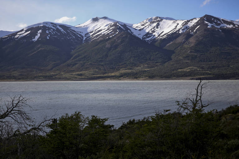 imagem bucólica mostra lago entre vegetação (em primeiro plano) e montanhas com picos de neve (ao fundo).