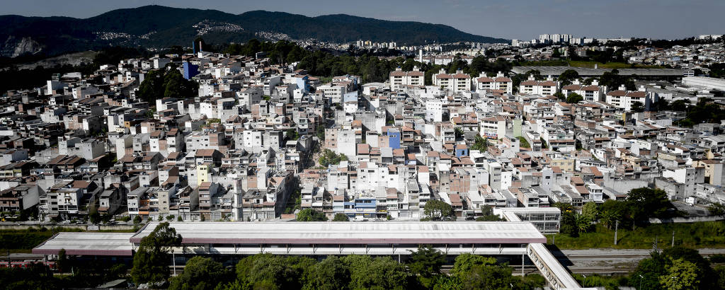 Imagem aérea mostra morro com diversas casas ao lado da estação ferroviária