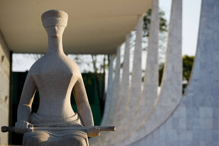 A escultura da Justiça, em concreto e em primeiro plano, com o prédio do STF ao fundo. É possível ver algumas das colunas do prédio do Supremo