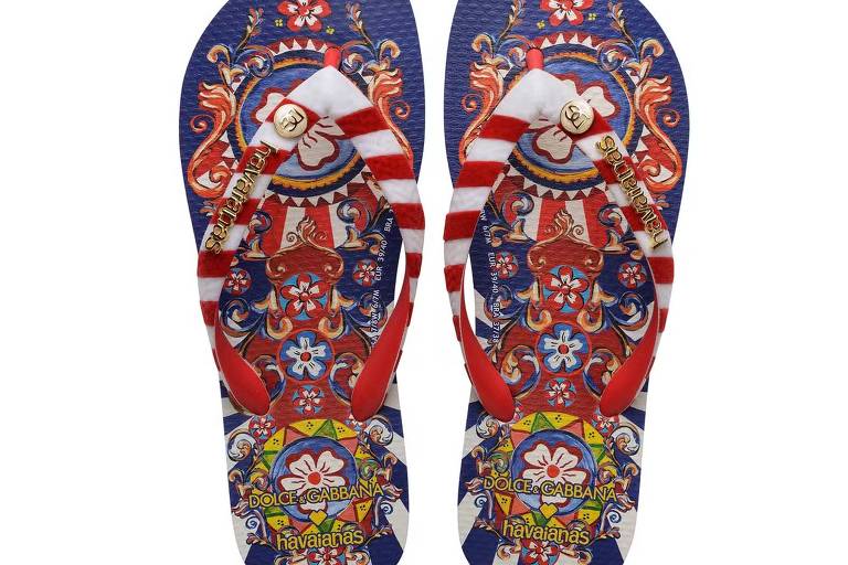 Um par de chinelos Havaianas com estampa colorida e vibrante em colaboração com a Dolce & Gabbana, exibindo um design rico em detalhes e cores, com predominância do vermelho, azul e amarelo, e adornado com o logotipo das marcas.