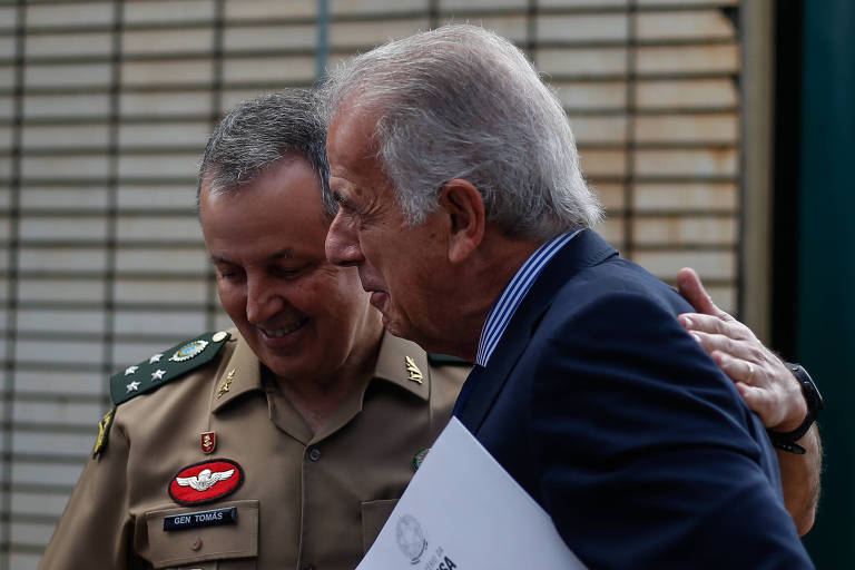 Tomás Paiva e José Múcio Monteiro, um em traje militar e outro em traje civil, compartilham um abraço, transmitindo uma sensação de respeito mútuo e camaradagem.