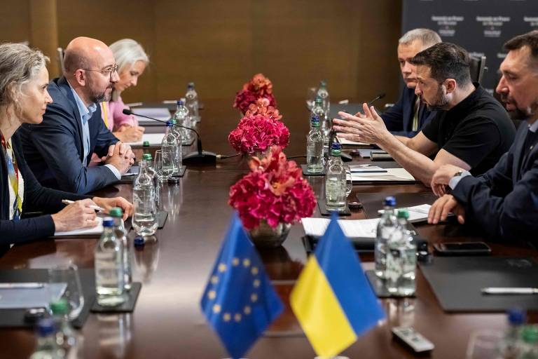 Vestindo uma camiseta preta, o presidente ucraniano gesticula sentado a uma mesa com outras cinco pessoas. De frente para ele, está Charles Michel