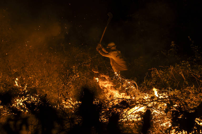 À noite, brigadistas usando roupas amarelas combatem incêndio florestal