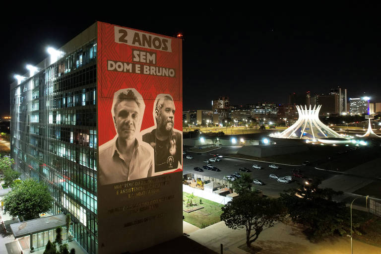 Projeção em empena de edifício com foto de Dom e Bruno e a mensagem '2 anos sem Dom e Bruno' fotografada à noite; ao fundo a catedral de brasília iluminada
