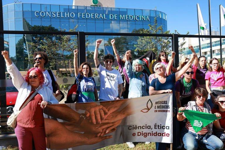 Mulheres protestando com cartazes em frente a prédio do CFM