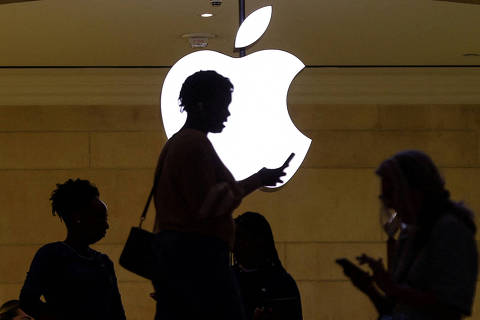 FILE PHOTO: A women uses an iPhone mobile device as she passes a lighted Apple logo at the Apple store at Grand Central Terminal in New York City, U.S., April 14, 2023. REUTERS/Mike Segar/File Photo ORG XMIT: FW1