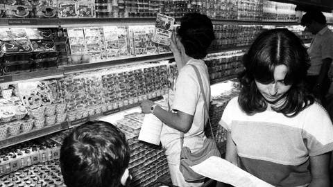 ORG XMIT: 204501_0.tif Com o congelamento dos preços, uma das medidas do Plano Cruzado, consumidores comparam os preços no supermercado com a tabela da Sunab. (São Paulo, SP, 25.03.1986. Foto: Jorge Araújo/Folhapress)