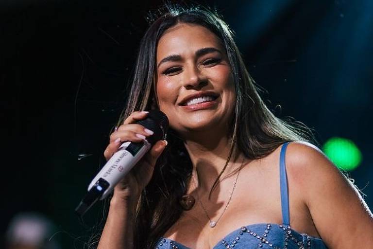 Em foto colorida, mulher aparece cantando em cima de um palco 