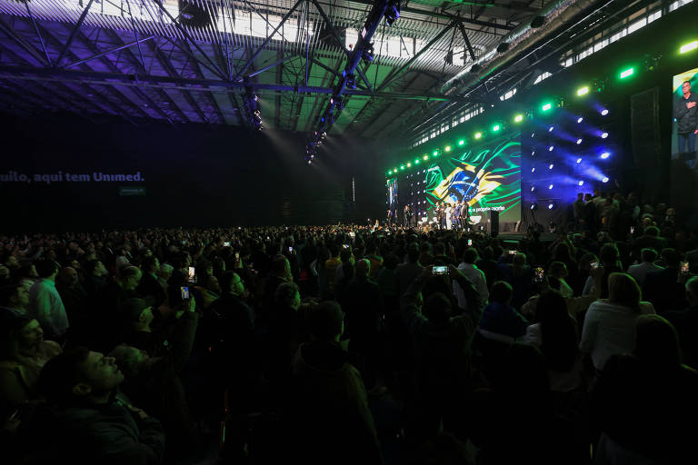 Pessoas em cima de palco com bandeira do Brasil ao fundo