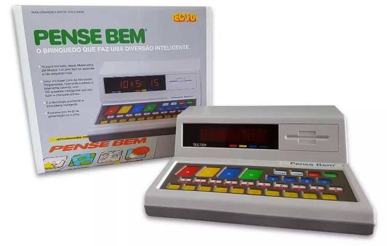 A imagem mostra o brinquedo educativo 'Pense Bem' da Tectoy, junto com sua caixa. O brinquedo é um dispositivo eletrônico com uma tela digital e vários botões coloridos, incluindo números e operações matemáticas. A caixa tem a inscrição 'Pense Bem - O brinquedo que faz uma diversão inteligente' e uma imagem do dispositivo. Há também um texto explicativo sobre o brinquedo na caixa.