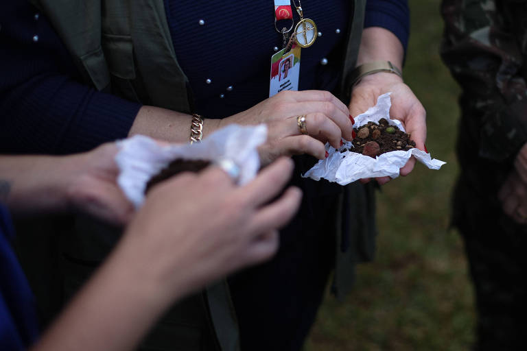 Na foto, duas pessoas seguram pequenas trouxinhas de papel contendo terra e sementes