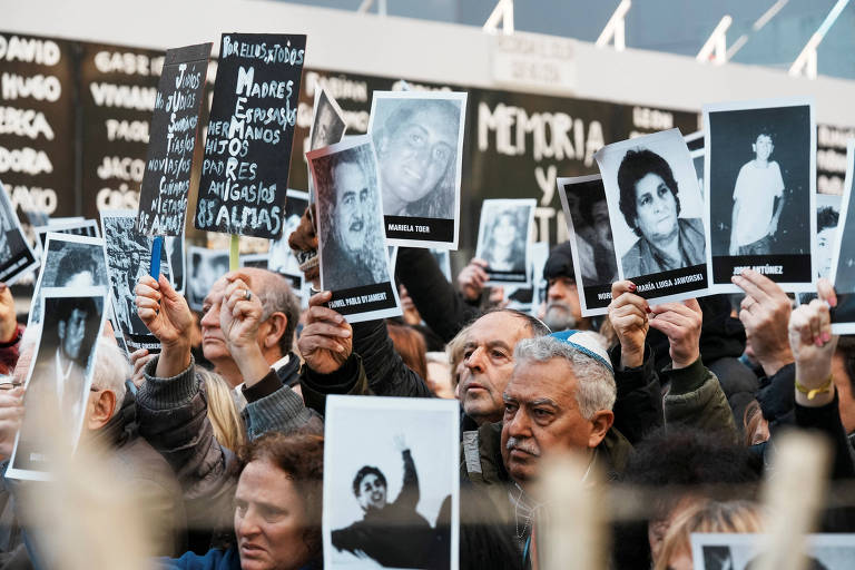Pessoas seguram imagens de vítimas do atentando contra a Amia em manifestação que marca os 30 anos do ataque, na capital Buenos Aires