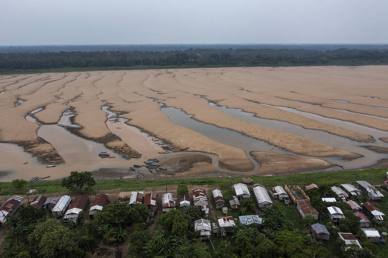 Casas na beira de um rio quase seco, visto de cima; há faixas com água, mas a maior parte do leito do rio está tomada por areia