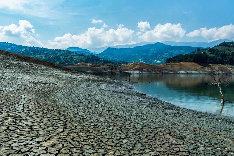 Lago com as margens secas, com a terra quebrada; a água é azulada