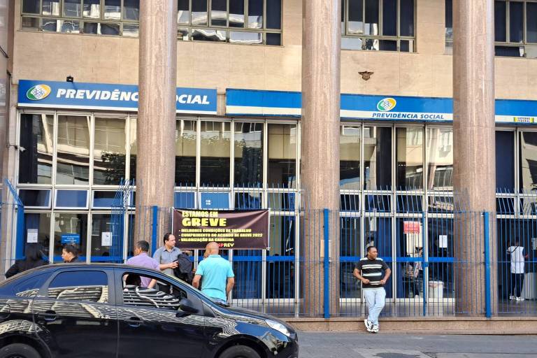 Fachada de agência do INSS tem cartaz sobre greve e carro preto estacionado na frente