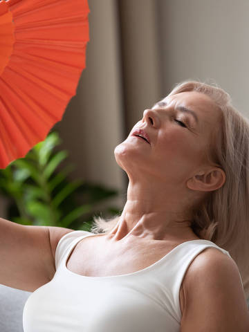 Exhausted older woman waving blue fan close up, suffering from heat, feeling unwell and uncomfortable, feeling uncomfortable, sweaty mature female cooling in hot summer weather, high temperature (Foto: Adobe Stock )