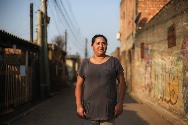 Na foto, uma mulher de camiseta cinza está de pé no meio de uma rua