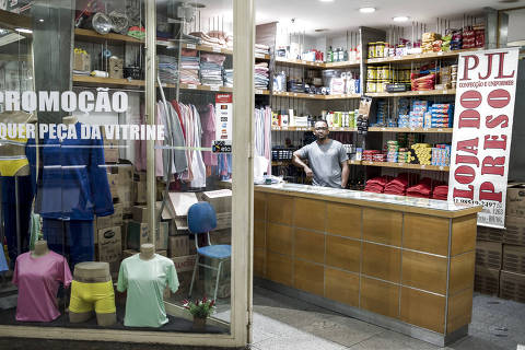 BELO HORIZONTE, MG, BRASIL, 2-09 -2024, 14:30h. Péricles Gomes Ribeiro, proprietário da Loja do Preso, no centro de Belo Horizonte coloca a placa que identifica o estabelecimento pelo nome. Para assegurar a descrição dos seus clientes, o proprietário preferiu não ter uma placa de identificação na fachada, e a faixa é colocada apenas para fotografias e reportagens. As iniciais PJL, que significam Paz, Justiça e Liberdade, estão em destaque tanto na fachada quanto no caraz. Regras duras de vestimenta e de alimentos que podem entrar em unidades prisionais criaram um nicho de mercado interessante. Negócios como a Loja do Preso enviam kits (os chamados jumbos) para as penitenciárias, com itens de higiene, cigarros, jogos e bíblias.  (Alexandre Rezende/Folhapress MERCADO) *** EXCLUSIVO FOLHA *** ORG XMIT: Alexandre Rezende