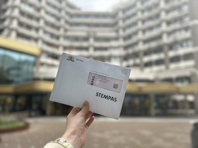 Voor het gebouw van de Tweede Kamer houdt iemand een stempas in een envelop omhoog.