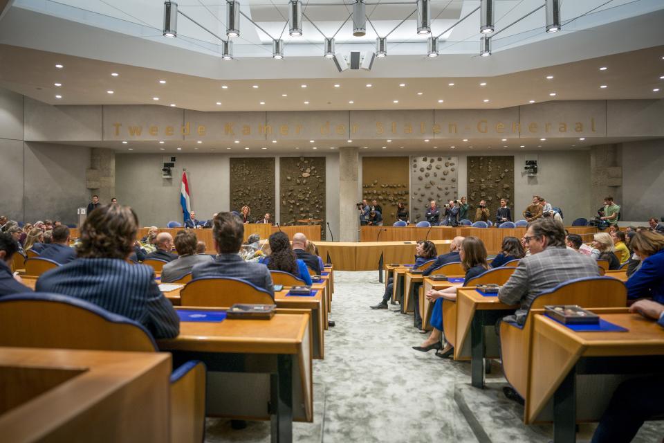 Volle plenaire zaal met Kamerleden op de rug gezien