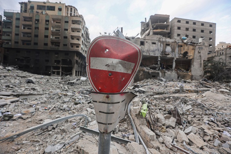 A damaged, bent no entry sign stands among a landscape of rubble and damaged buildings in Gaza.