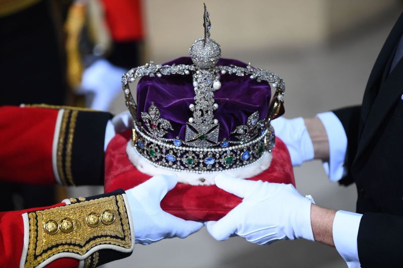 A purple crown with jewels is passed between hands.