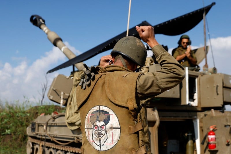 An Israeli soldier wearing a patch on the back of his flack jacket showing Lebanon's Hezbollah leader Hassan Nasrallah as a target, stands in front of a self-propelled artillery howitzer in Upper Galilee in northern Israel on January 4, 2024.