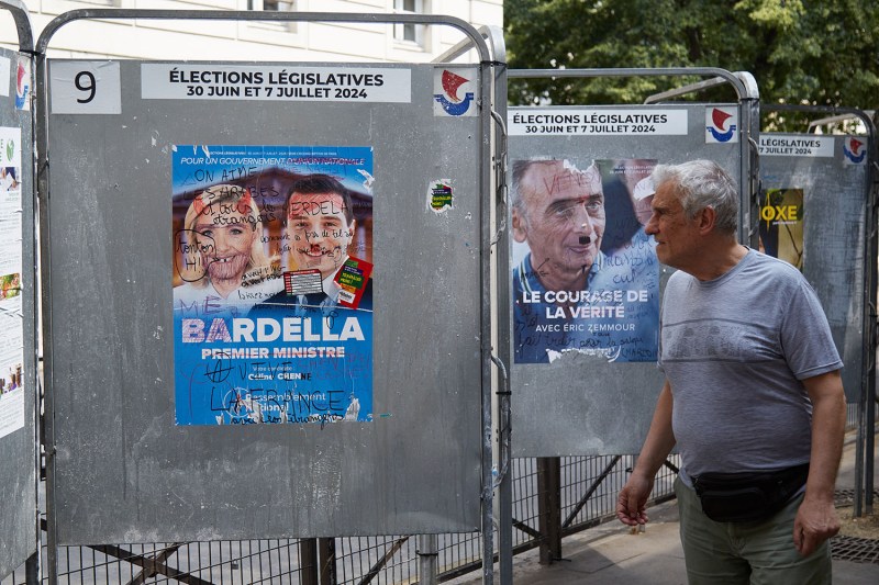 A pedestrian passes vandalized European Parliament election posters of Marine Le Pen and Jordan Bardella of the National Rally party on a street in Paris on June 27.