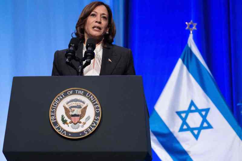 U.S. Vice President Kamala Harris delivers a speech while standing behind a podium at an Israeli Embassy event in Washington, D.C. The seal of the United States is affixed to the podium, and an Israeli flag hangs behind Harris.