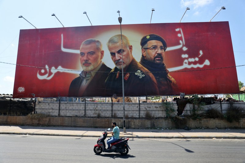 A man rides his moped past a billboard bearing portraits of slain leaders, Ismail Haniyeh of the Palestinian militant group Hamas, Iranian Quds Force chief Qasem Soleimani, and Hezbollah senior commander Fuad Shukr on the main road near the Beirut International Airport on August 3, 2024.