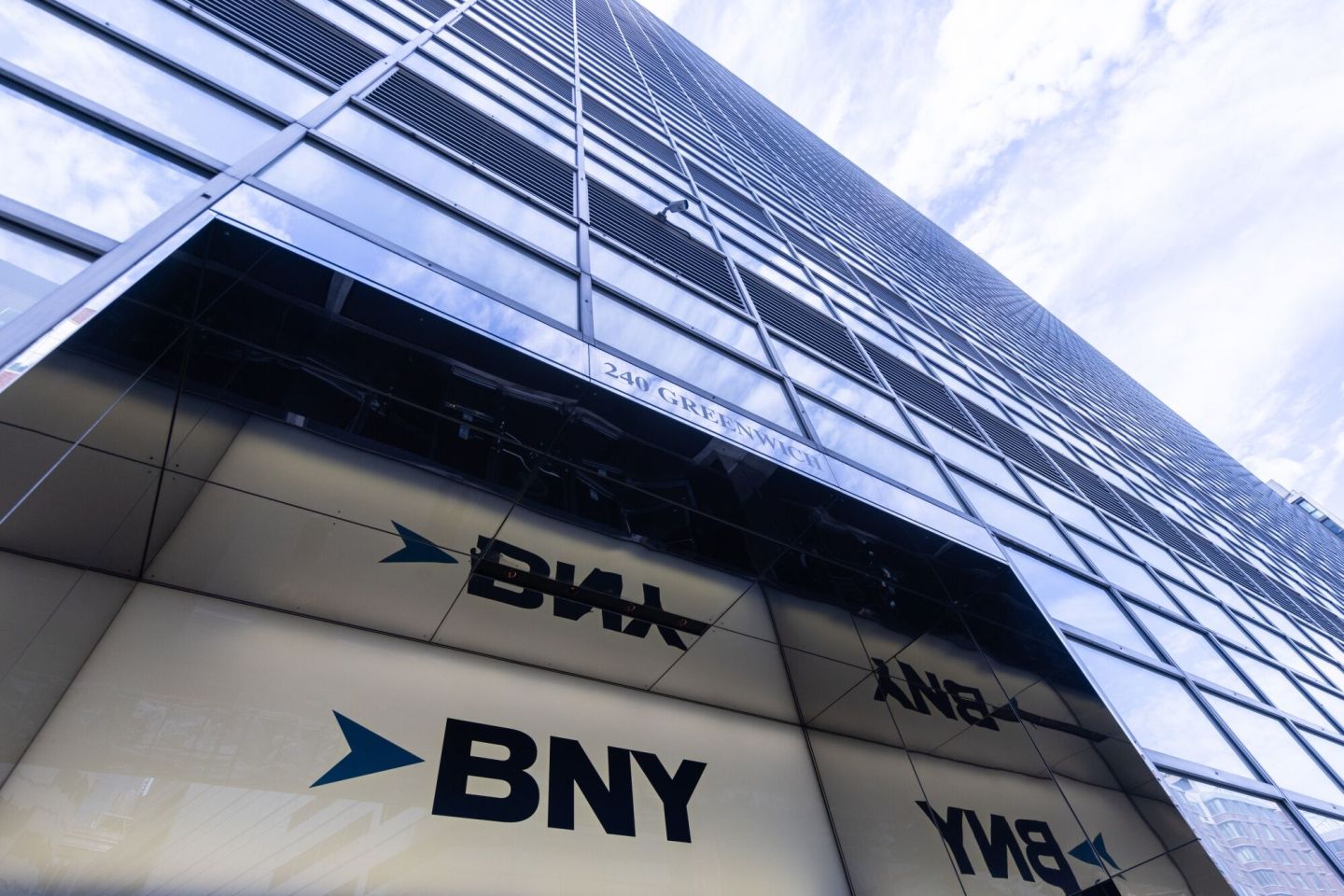 An image looking up a a sky scraper, with the BNY logo in a doorway at the bottom and clouds at the top.