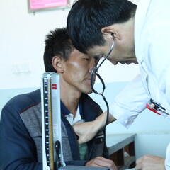 A doctor examines a patient using a stethoscope in a barren room in rural China.