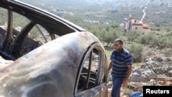资料照片：2023年12月3日，一名巴勒斯坦男子在以色列占领的约旦河西岸萨尔菲特附近检查一辆在以色列定居者突袭中被烧毁的汽车。（路透社照片）