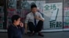 一名男子坐在北京一座商业楼张贴的打折广告前。(2024年5月27日)