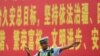 (FILE) A police officer gesturing in front of a propaganda billboard urging "the maintenance of rule of law in Xinjiang" on a road in China's northwestern Xinjiang region, July 19, 2023.