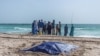 TOPSHOT - Bystanders look at covered bodies of migrants who perished in a shipwreck off the coast of Mauritania while on a beach outside Nouakchott on July 24, 2024.