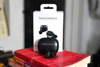 Shot of Bowers & Wilkins Pi8 earbuds with charging case and box on top of red book.