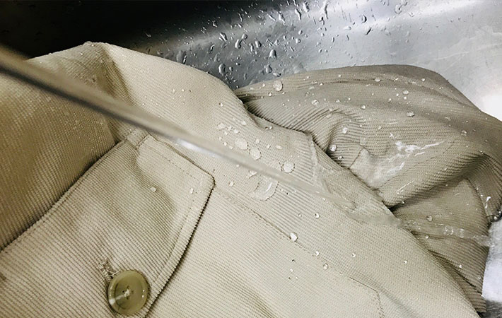 台所の蛇口をひねって水道水を超撥水２WAYシェフジャケットにかけている