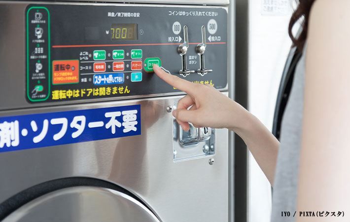 コインランドリーのボタンを押す女性の写真