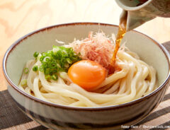 うどんに麺つゆをかける写真