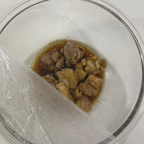 調味料を絡めた鶏もも肉の入ったボウルにラップをかける様子