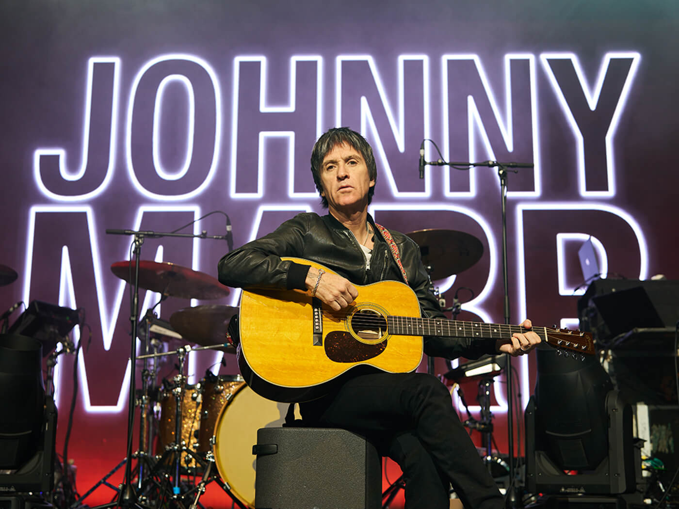 Johnny Marr with his signature Martin guitar on a stage with his name in the background, photo by Martin