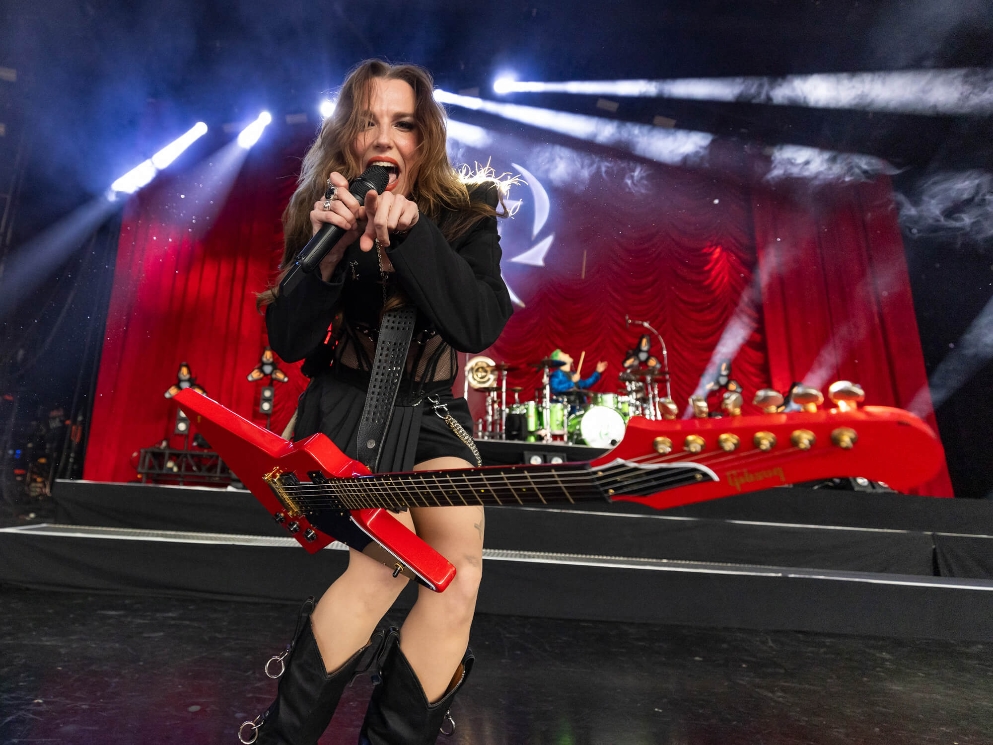 Lzzy Hale. She is performing live on stage and has a mic in one hand, and is pointing at the camera with the other.