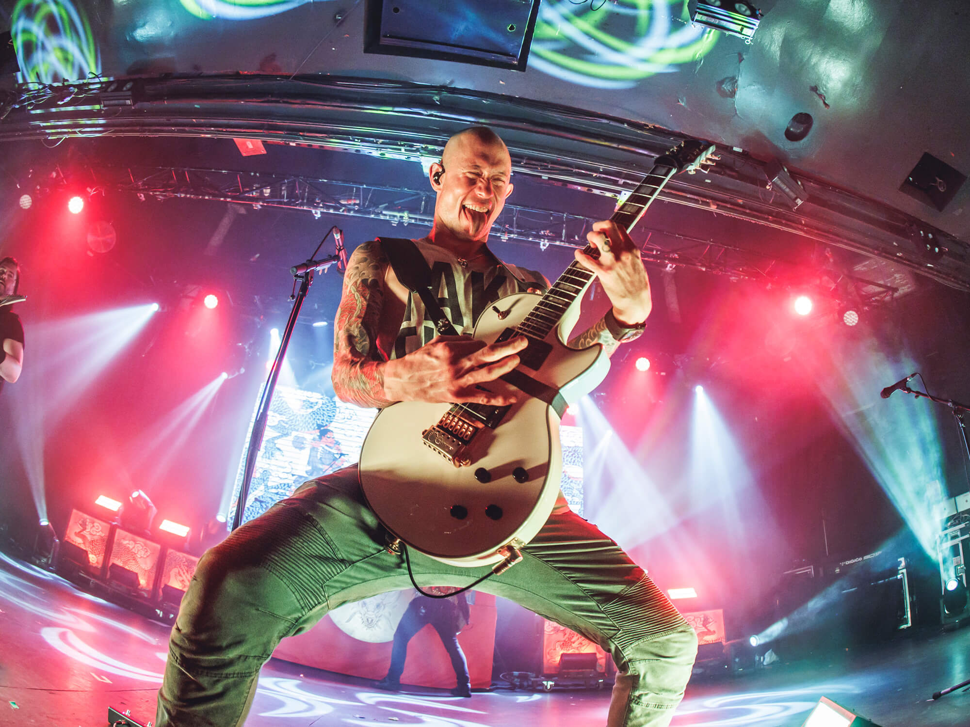 Matt Heafy on stage. He is holding his guitar upright as he's playing its and it pulling a playful facial expression with his tongue out.