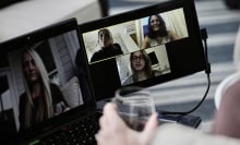 a person holding a class of water looks at a dual monitor video call