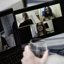 a person holding a class of water looks at a dual monitor video call