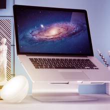 Laptop on a computer stand surrounded by a bowl-shaped light, a scented candle, and a plant