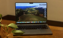 A 14-inch MacBook Pro sitting on a table next to a plant.