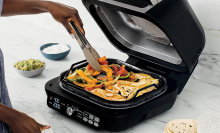 Person's hand using tongs to cook vegetables and chicken on Ninja griddle